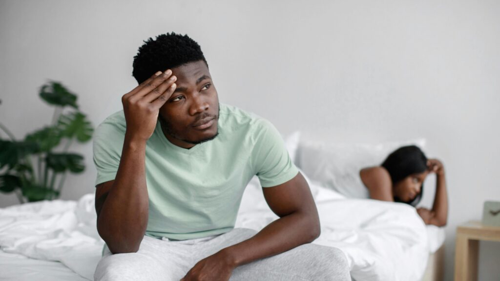 Man looking thoughtful on bed, considering does porn cause premature ejaculation.